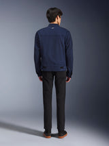 Giacca Alpinestars Bruiser in blu scuro, vista posteriore su modello, giacca da moto in tessuto dal design ispirato al workwear, con un piccolo logo bianco sul colletto posteriore e linguette di regolazione in vita, abbinata a pantaloni neri