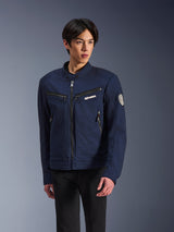 Alpinestars Bruiser Jacket, giacca da moto in tessuto blu scuro, indossata da un uomo con pantaloni neri, con tasche con zip, logo Alpinestars bianco sul petto e patch circolare Oscar a spirale sulla manica, stile urban streetwear per motociclisti