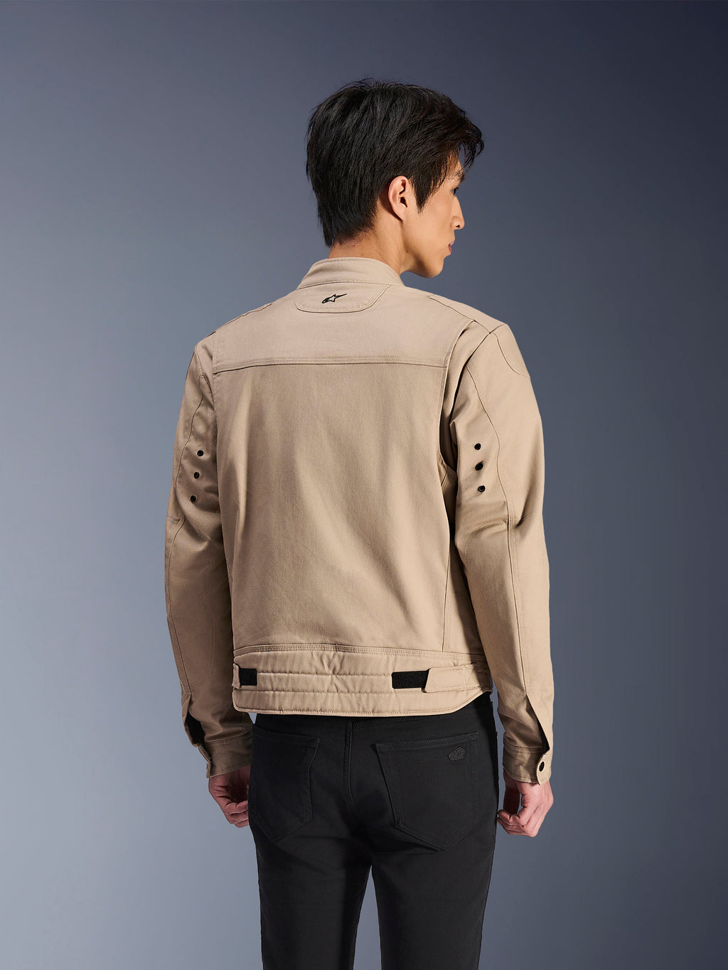 Giacca Alpinestars Bruiser, giacca da moto urbana marrone, vista posteriore che mostra le spalle plissettate articolate e i regolatori in vita, indossata con pantaloni neri, abbigliamento da moto contemporaneo ispirato allo stile workwear