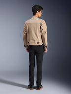 Vista posteriore di un modello che indossa la giacca Alpinestars Bruiser in marrone, una giacca da moto urbana dal design ispirato all'estetica workwear, con dettagli di occhielli in metallo sulla schiena e regolatori in vita, abbinata a pantaloni neri e sneaker, stile street riding contemporaneo.