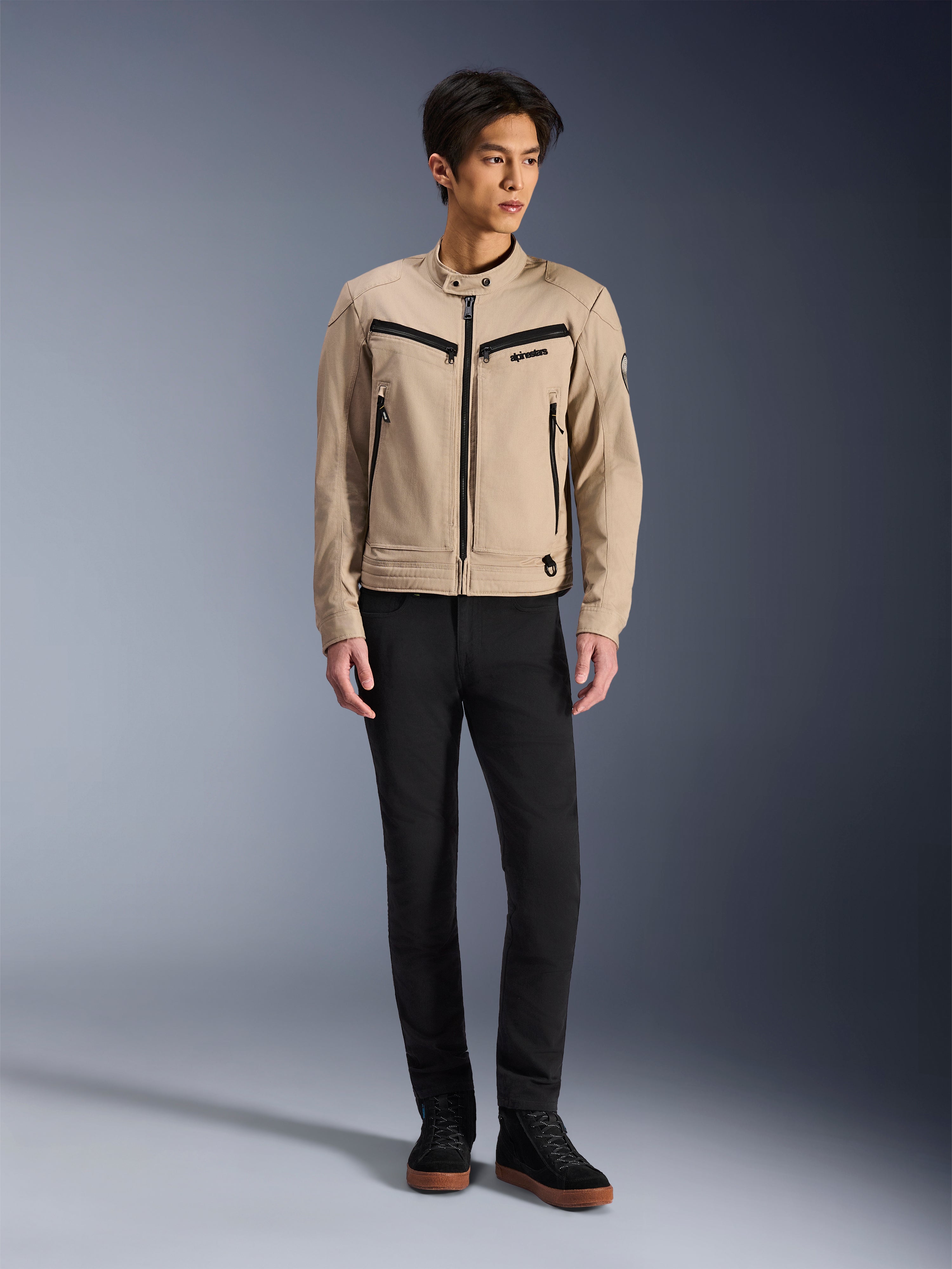 Giacca Alpinestars Bruiser, giacca da moto urbana color Aluminum, indossata con pantaloni neri e sneaker nere, caratterizzata da tasche nere con zip e colletto con bottone a pressione, design contemporaneo ispirato al workwear per la guida urbana