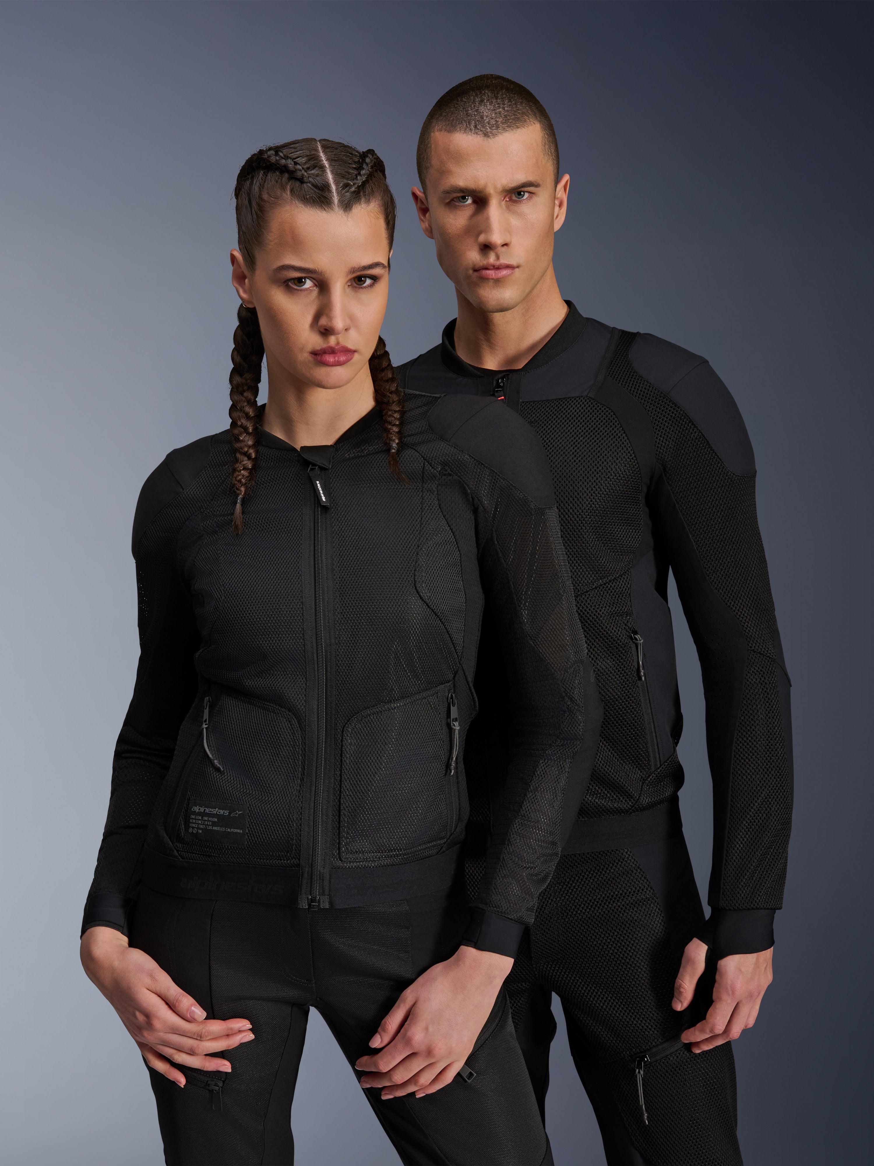 Giacca Alpinestars Troop-Air Pro, giacche tecniche corazzate nere indossate da modelli uomo e donna, con pannelli in mesh traspirante e protezioni integrate, abbigliamento da moto urban progettato per la guida in climi caldi.