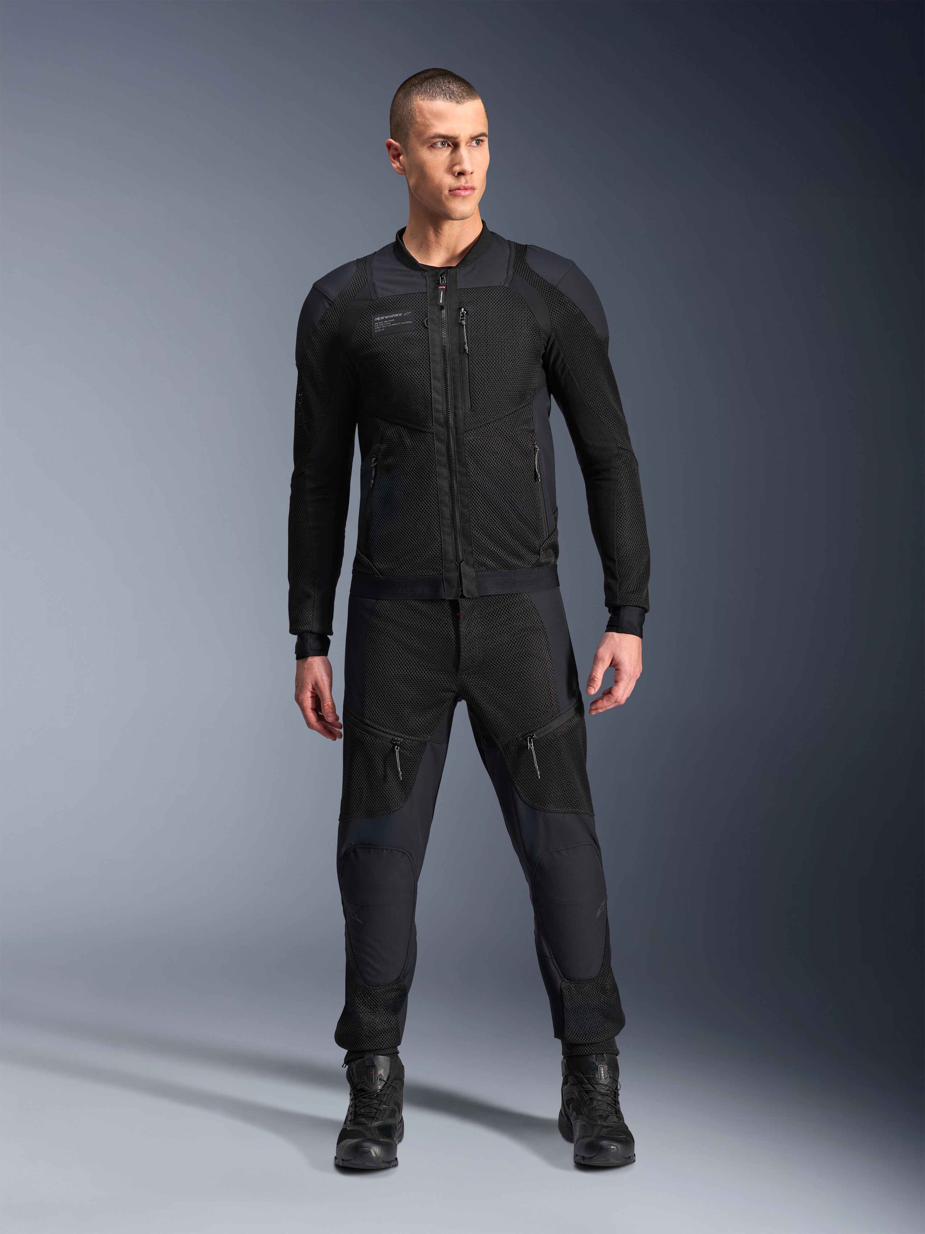 Giacca Alpinestars Troop-Air Pro, giacca tecnica da moto corazzata nera, caratterizzata da pannelli in mesh e cerniere frontali, indossata con pantaloni neri coordinati e stivali da guida, abbigliamento stradale urbano premium