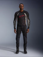Modello che indossa la giacca Alpinestars Troop-Air Jacket in Black Ash Gray e Bright Red, giacca da moto tecnica in mesh con un evidente logo rosso sul petto, abbinata a pantaloni e stivali da moto neri, abbigliamento per la guida urbana.
