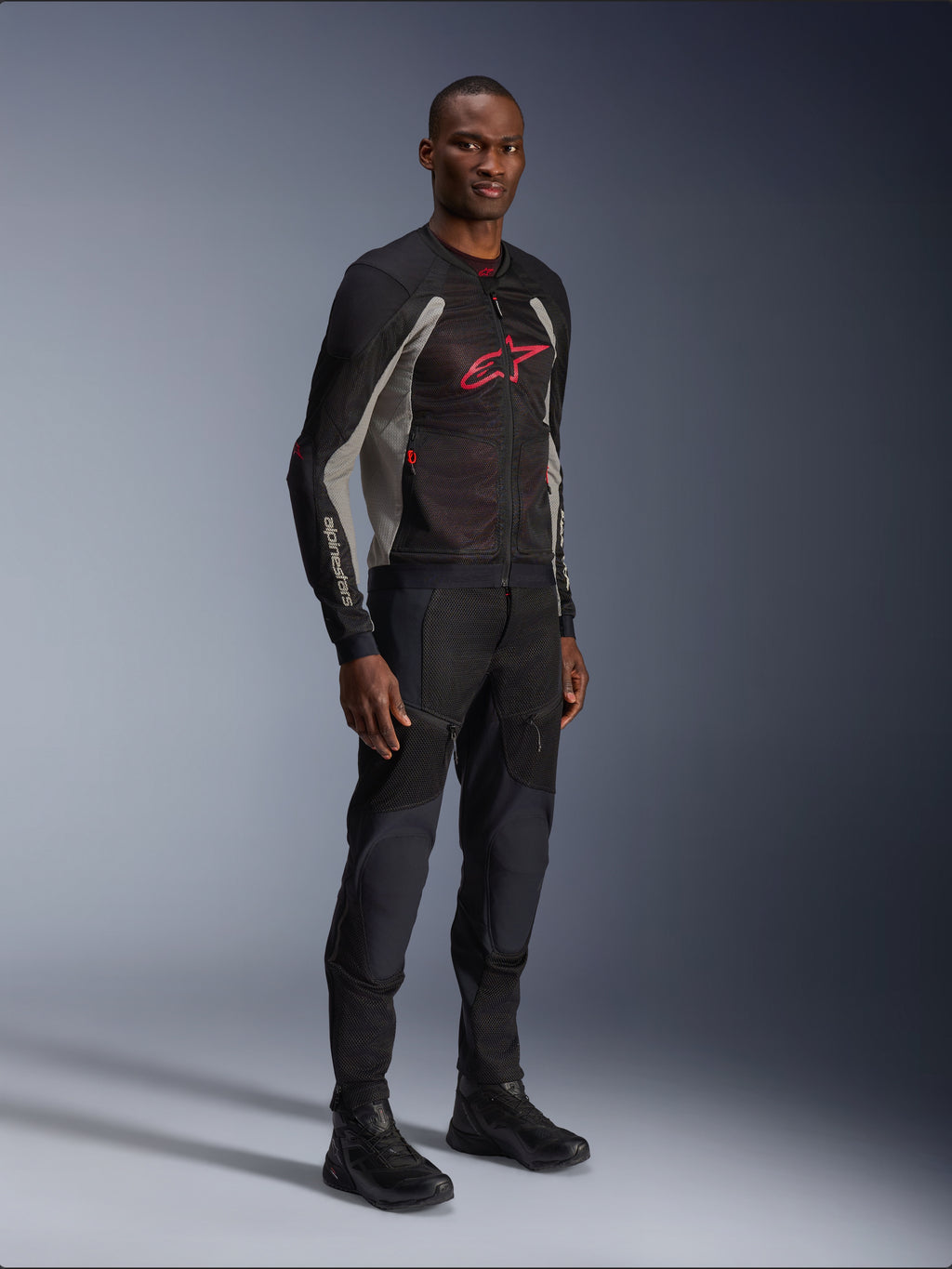 Giacca Alpinestars Troop-Air, giacca da moto tecnica in mesh in nero, grigio cenere e rosso acceso, indossata da un modello con pantaloni e stivali neri abbinati, con logo Alpinestars rosso sul petto, abbigliamento da moto urban contemporary