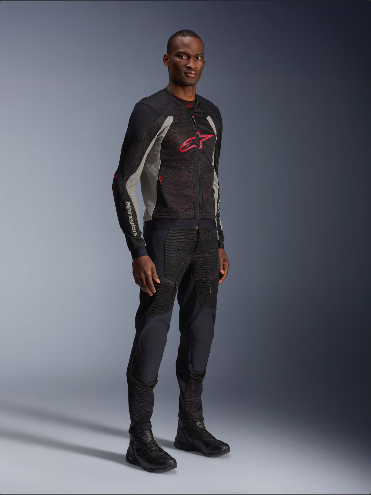 Giacca Alpinestars Troop-Air, giacca da moto tecnica in mesh in nero, grigio cenere e rosso acceso, indossata da un modello con pantaloni e stivali neri abbinati, con logo Alpinestars rosso sul petto, abbigliamento da moto urban contemporary