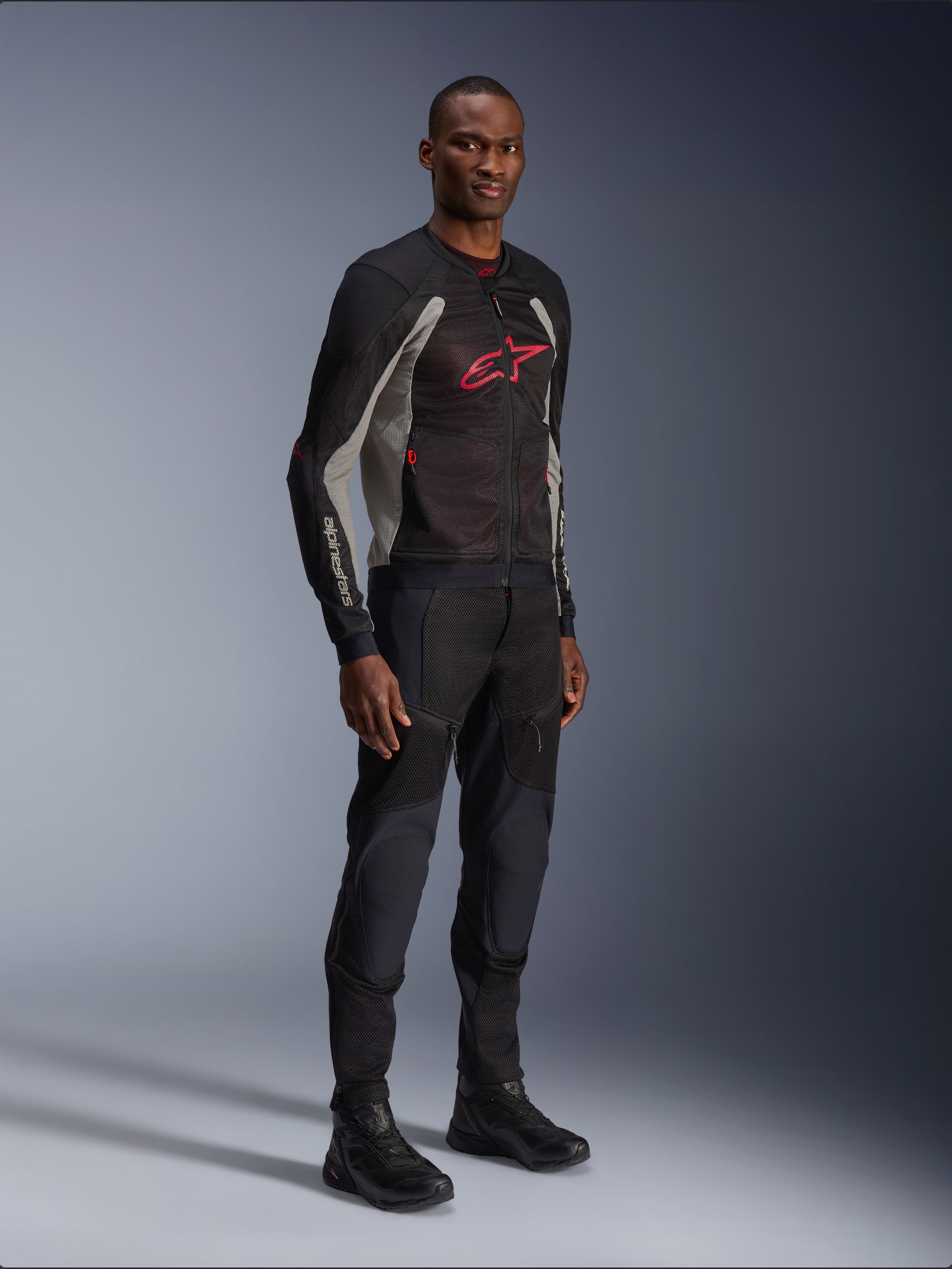Giacca Alpinestars Troop-Air, giacca da moto tecnica in mesh in nero, grigio cenere e rosso acceso, indossata da un modello con pantaloni e stivali neri abbinati, con logo Alpinestars rosso sul petto, abbigliamento da moto urban contemporary
