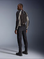 Modello che indossa la giacca Alpinestars Troop-Air vista da dietro, nero e grigio cenere con accenti rosso brillante, costruzione in mesh tecnica per la ventilazione, abbinata a pantaloni da moto neri e stivali da guida, stile urban contemporaneo