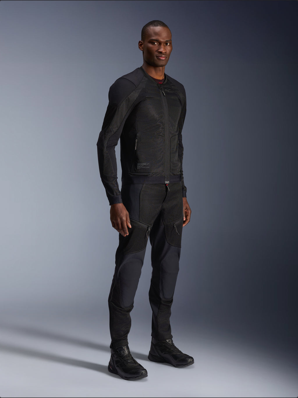 Alpinestars Troop-Air Jacket, nera, giacca da moto in mesh tecnico indossata da un modello con pantaloni e stivali neri coordinati, con struttura in mesh leggero e design urbano minimalista