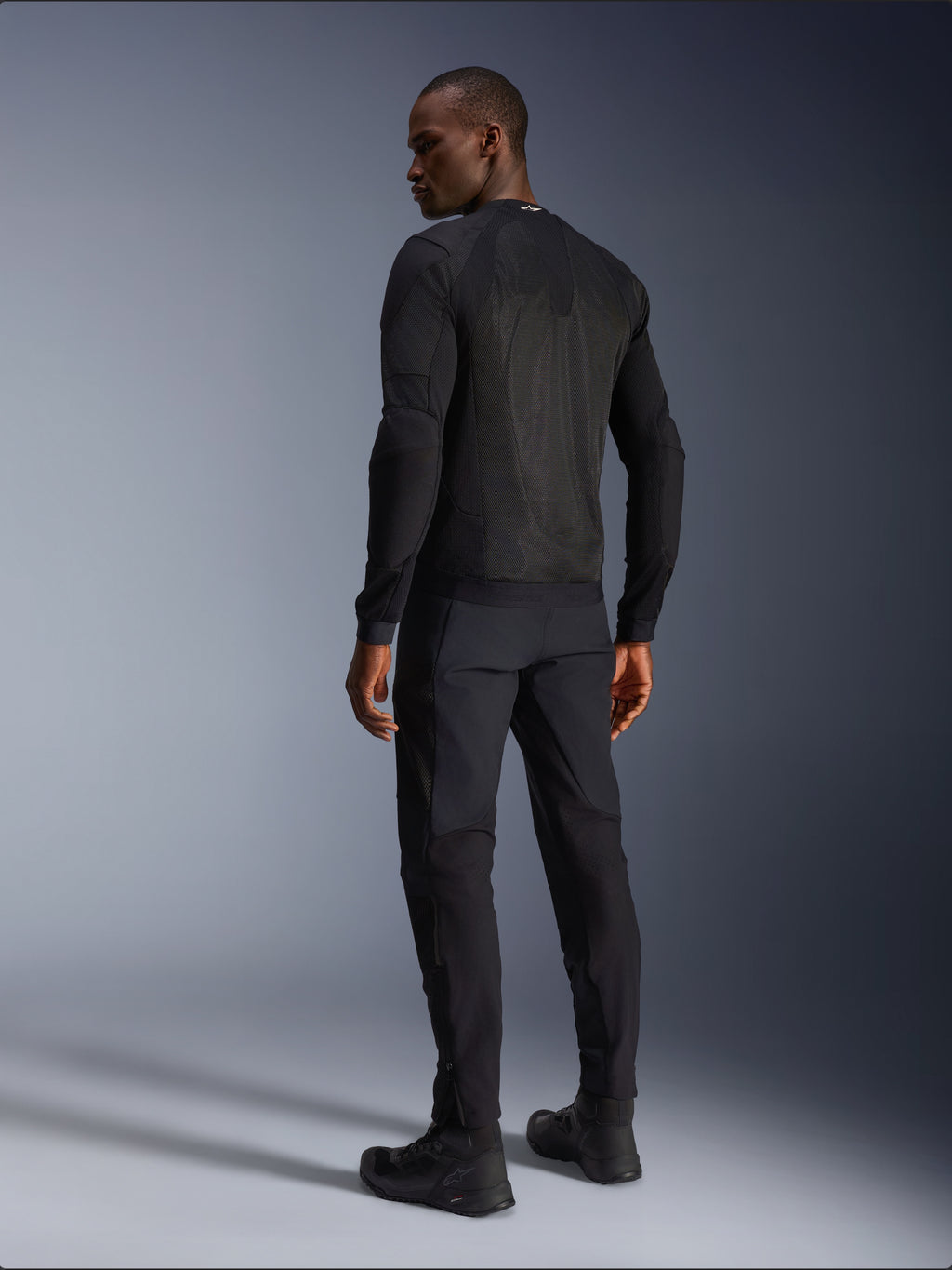 Alpinestars Troop-Air Jacket, giacca tecnica da moto ventilata nera, vista posteriore con ampi pannelli in mesh per una ventilazione superiore, indossata con pantaloni neri coordinati e stivali da guida, design urbano contemporaneo per la guida estiva.