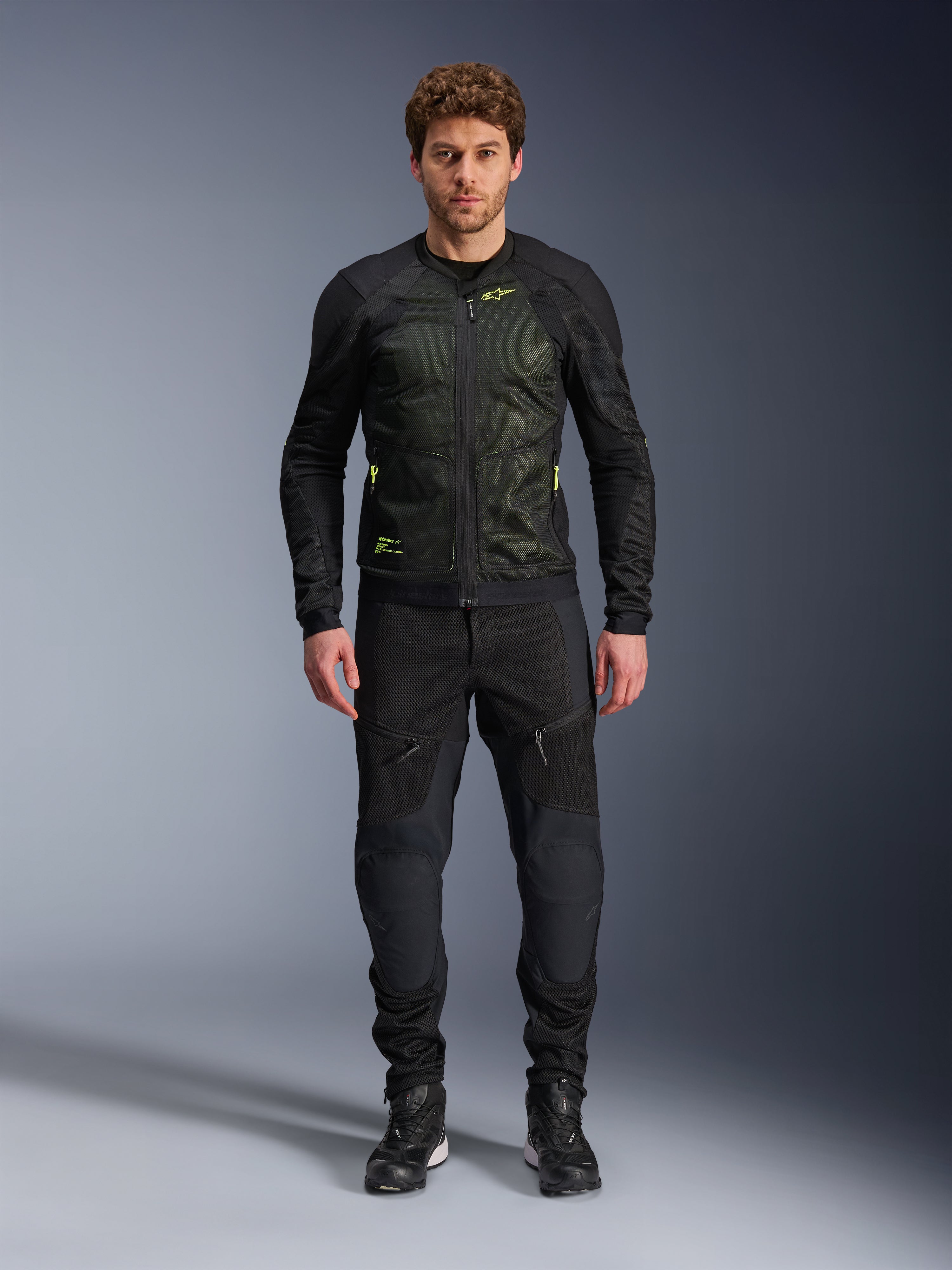 Modello che indossa la giacca Alpinestars Troop-Air in Nero Giallo Fluo, con pannelli in mesh tecnico e accenti giallo brillante, abbinata a pantaloni da moto e scarpe neri, abbigliamento da moto contemporaneo per climi caldi