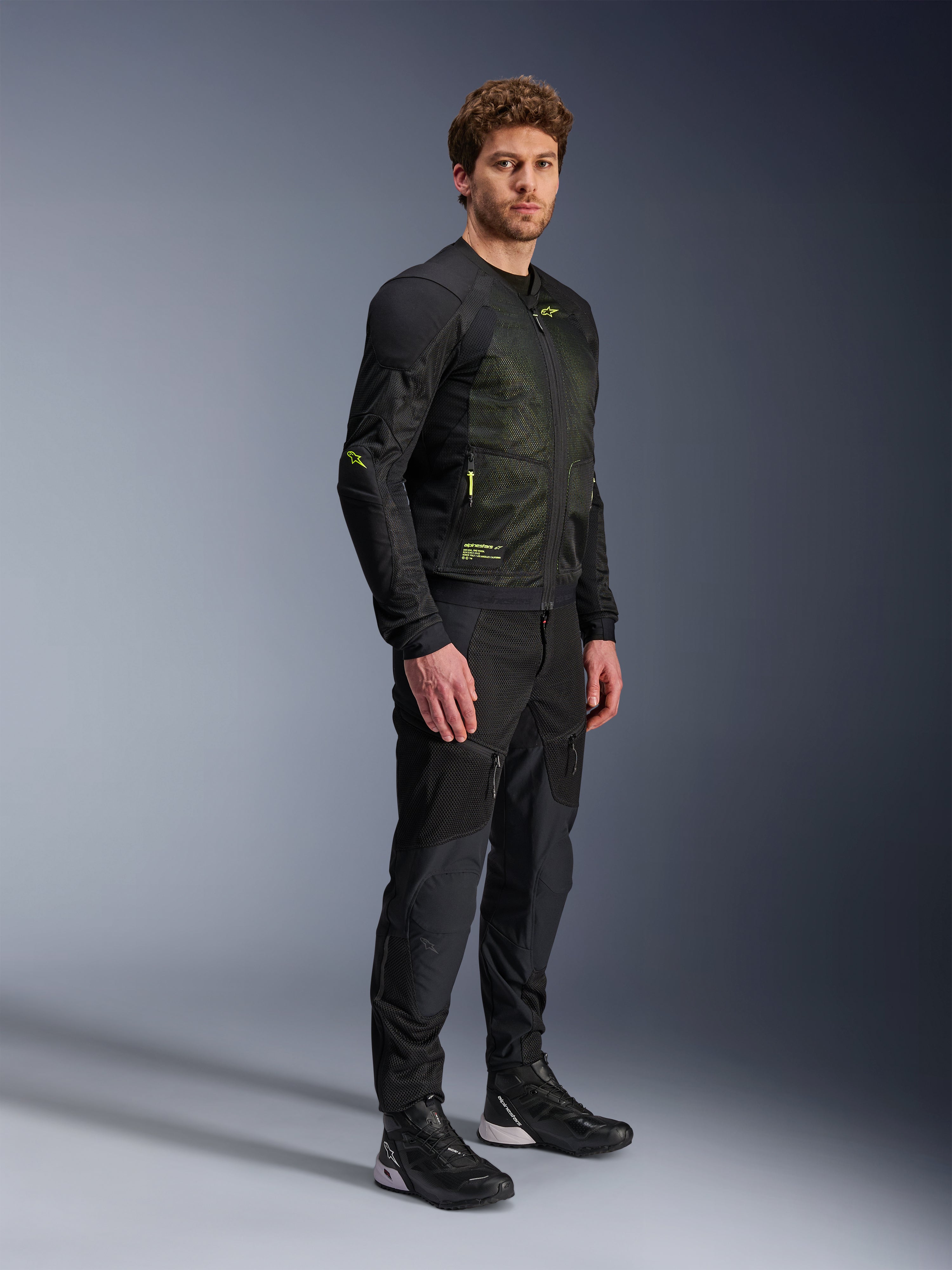 Giacca Alpinestars Troop-Air, giacca moto in mesh, nero e giallo fluo, indossata da un modello con pantaloni neri e scarpe da moto coordinati, caratterizzata da una struttura in mesh ad alto flusso d'aria con accenti giallo fluorescente su petto e maniche, design tecnico leggero per la guida su strada