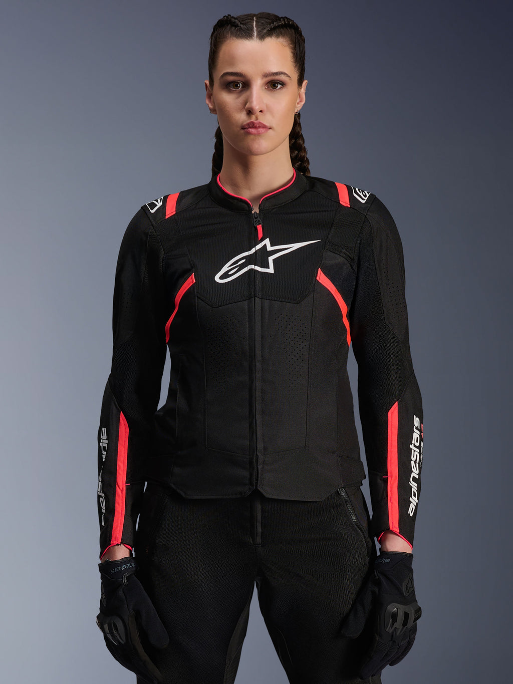 Giacca Alpinestars Stella T-Sps Air V2 da donna, nero e Diva Pink, giacca da moto in tessuto con pannelli in mesh traspirante e accenti rosa, logo Alpinestars bianco sul petto, indossata da una modella con pantaloni e guanti da guida neri.