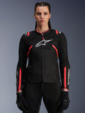 Giacca Alpinestars Stella T-Sps Air V2 da donna, nero e Diva Pink, giacca da moto in tessuto con pannelli in mesh traspirante e accenti rosa, logo Alpinestars bianco sul petto, indossata da una modella con pantaloni e guanti da guida neri.