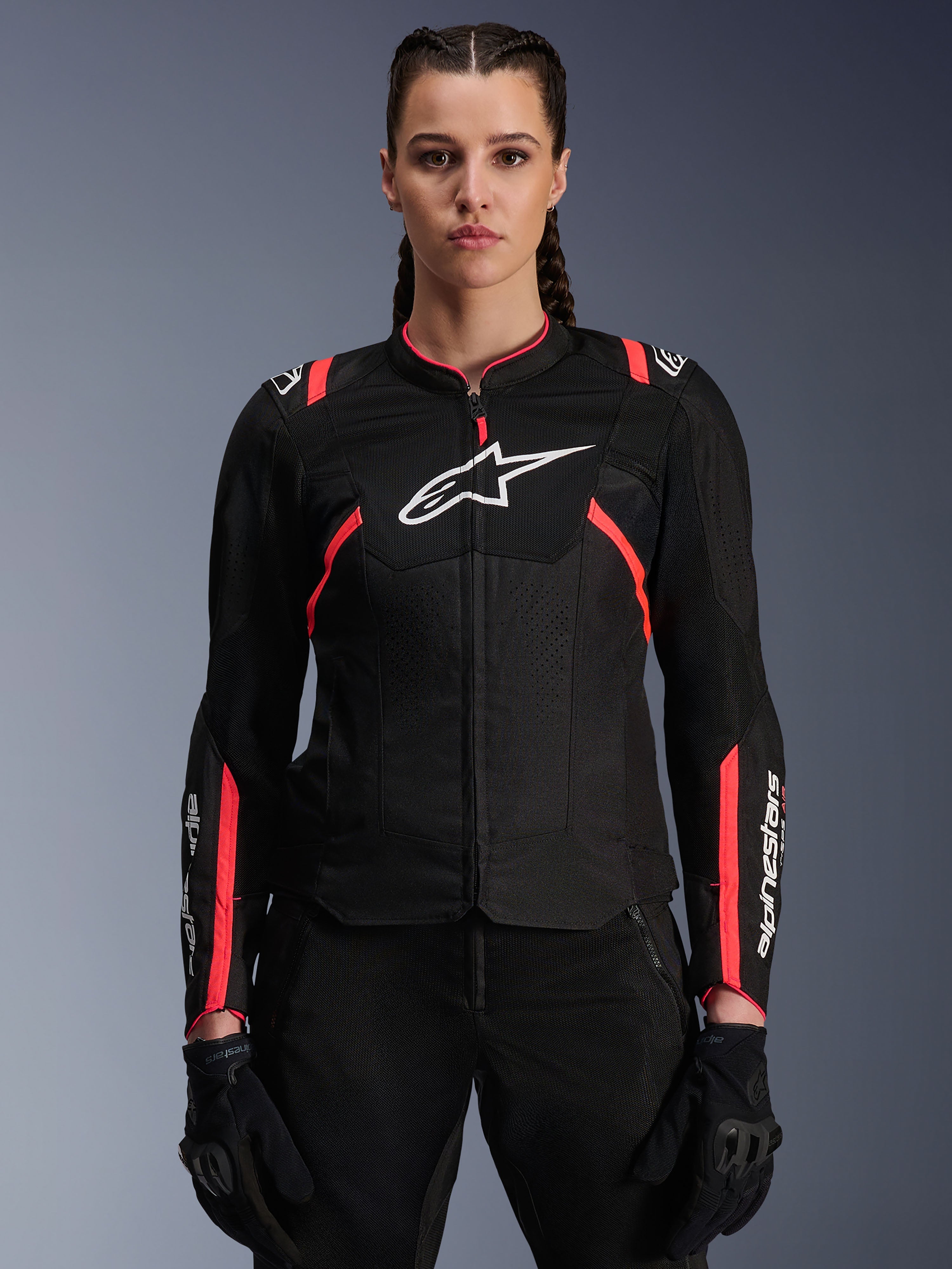 Giacca Alpinestars Stella T-Sps Air V2 da donna, nero e Diva Pink, giacca da moto in tessuto con pannelli in mesh traspirante e accenti rosa, logo Alpinestars bianco sul petto, indossata da una modella con pantaloni e guanti da guida neri.