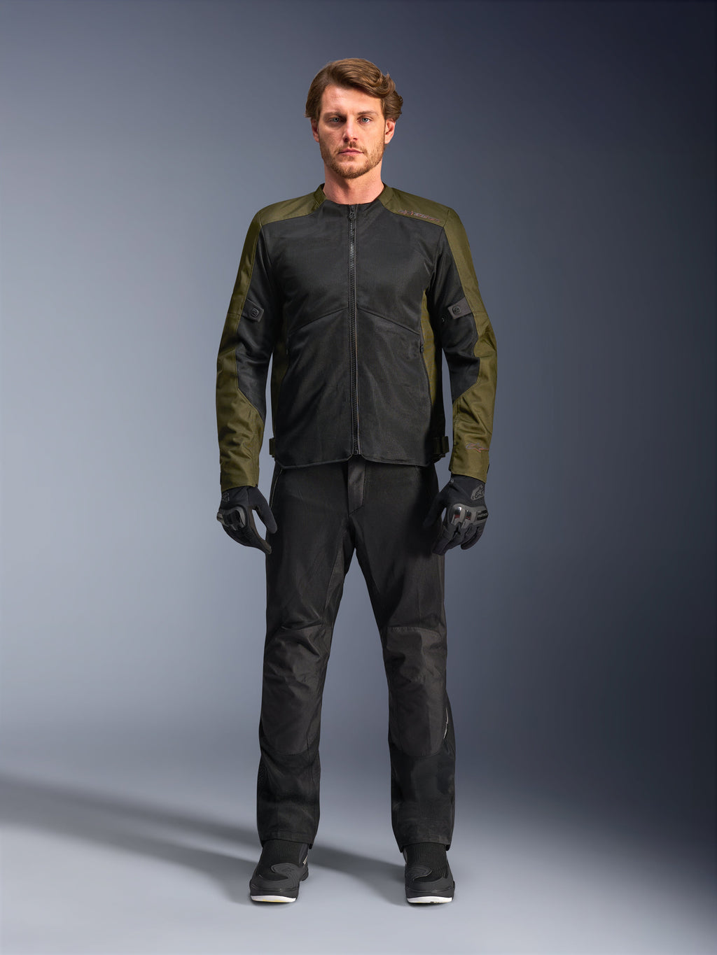 Giacca Alpinestars C-1 Air, kaki e nero, indossata da un modello con pantaloni da moto e guanti neri, design in tessuto leggero con pannelli in mesh tecnica, abbigliamento urbano contemporaneo per motociclisti