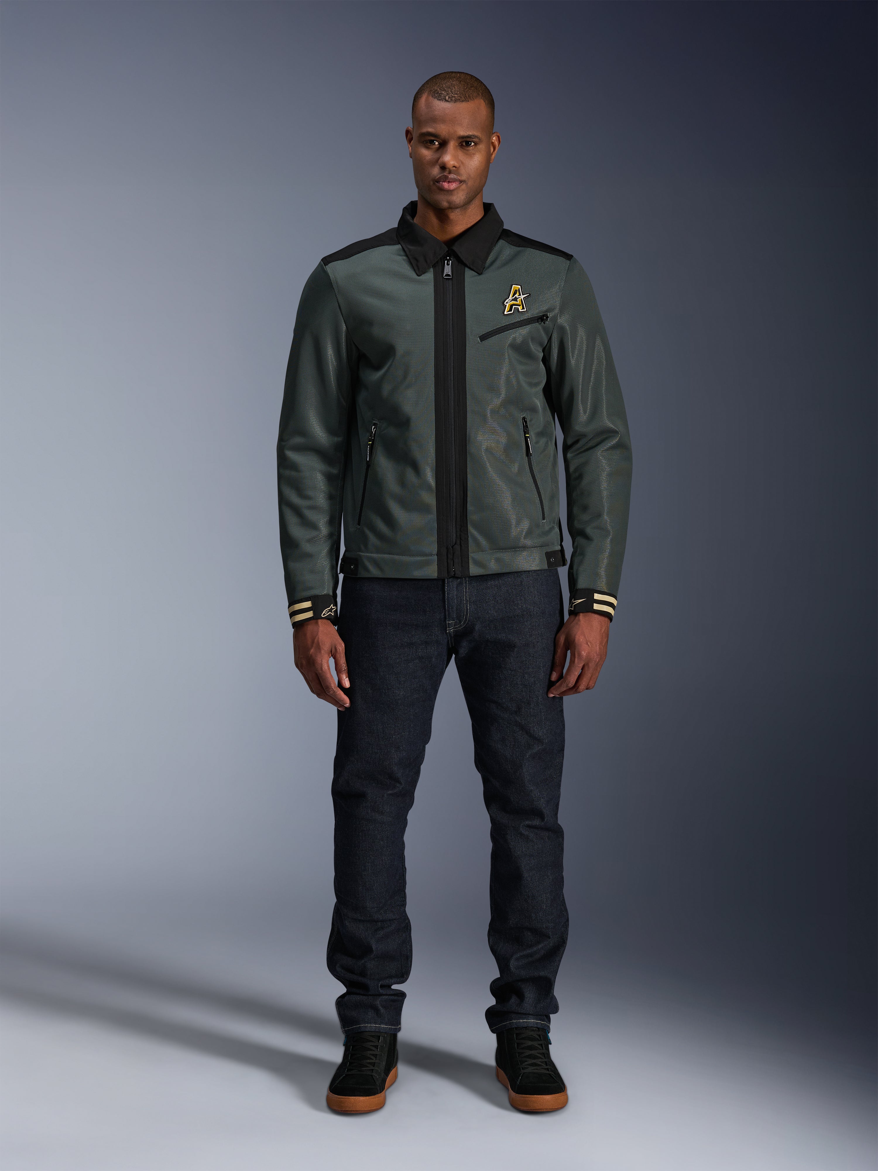 Giacca Alpinestars Ignite Air in Urban Gray Black Blue, giacca da moto stile Harrington con colletto a camicia e costruzione in rete, indossata da un uomo con jeans in denim scuro e sneakers nere, streetwear urbano per motociclisti.