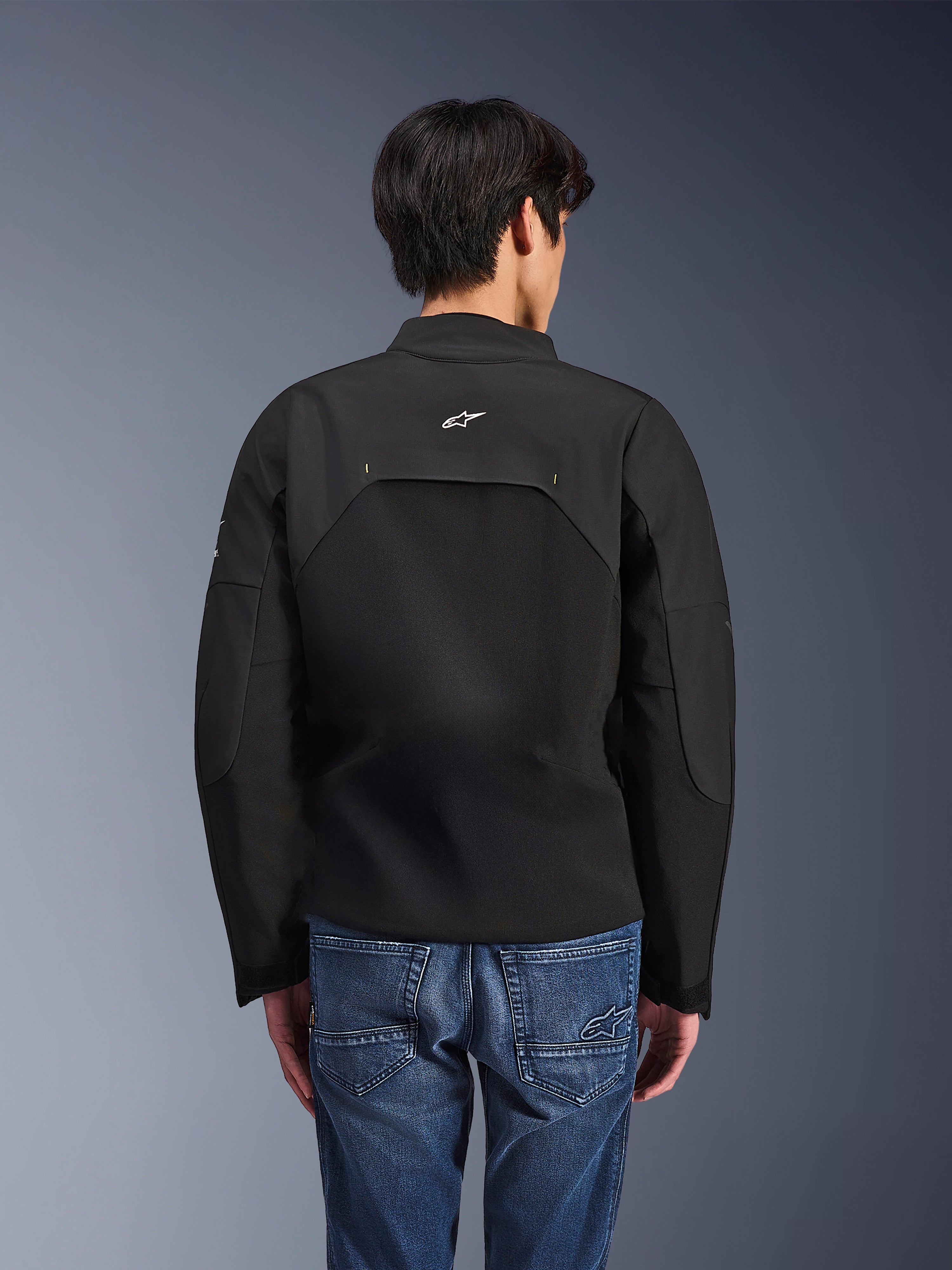 Giacca Alpinestars Provoke, giacca da moto urbana, nero, vista posteriore con logo Astars bianco e pannelli tecnici in ripstop, indossata con jeans in denim blu, design contemporaneo per il commuting cittadino