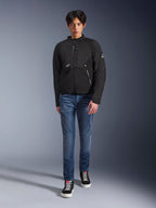 Modello maschile che indossa la giacca Alpinestars Provoke in nero, giacca da moto urbana in tessuto con cerniere tecniche e pannelli in softshell ripstop, abbinata a jeans blu e sneakers nere, stile urban rider contemporaneo.