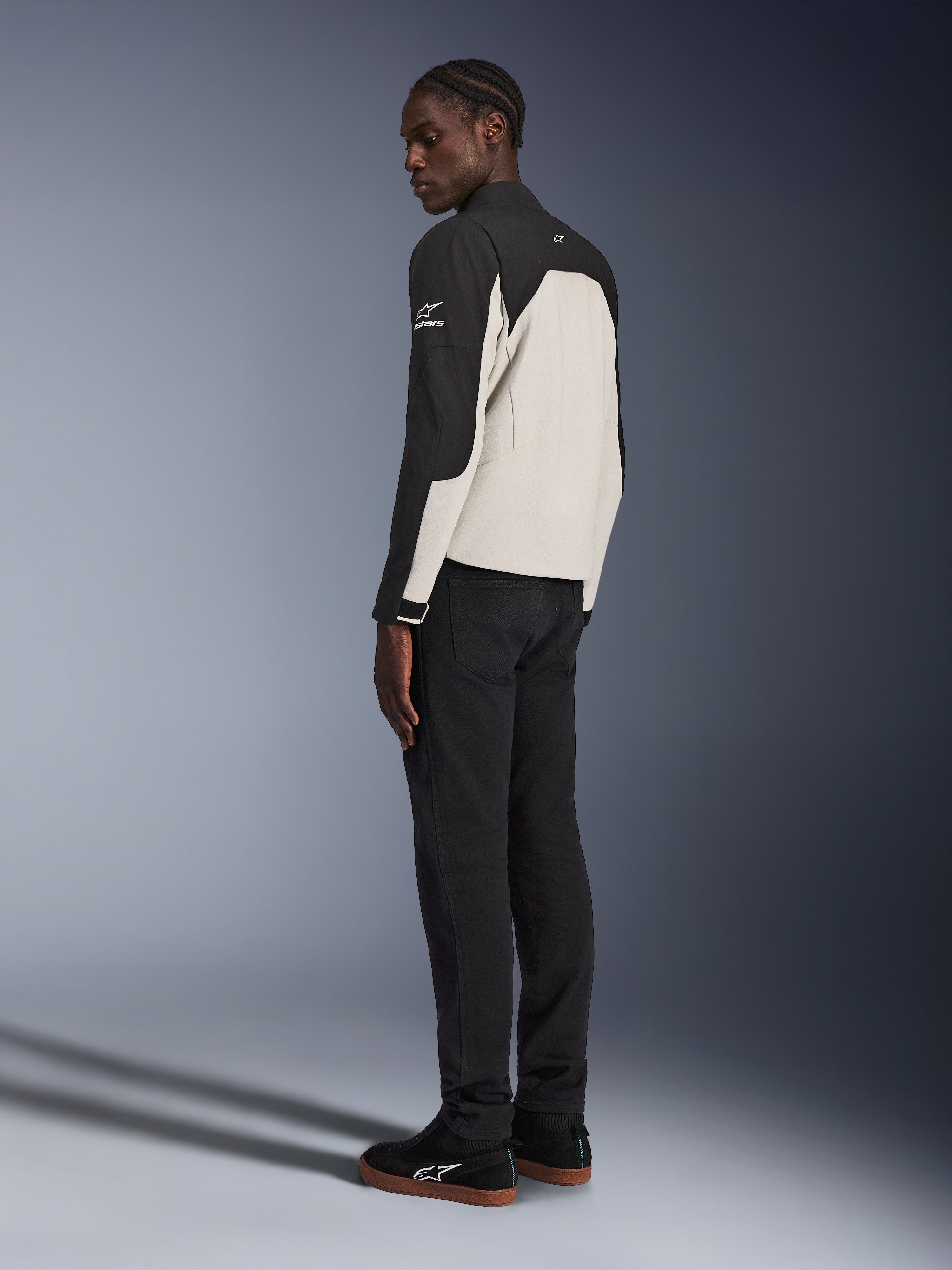Giacca Alpinestars Provoke, giacca da moto urbana, Nero e Grigio Metallo, vista posteriore di tre quarti su un modello, costruzione in tessuto bicolore con logo Alpinestars sulla spalla, indossata con pantaloni neri e sneakers nere, protezione contemporanea street-ready