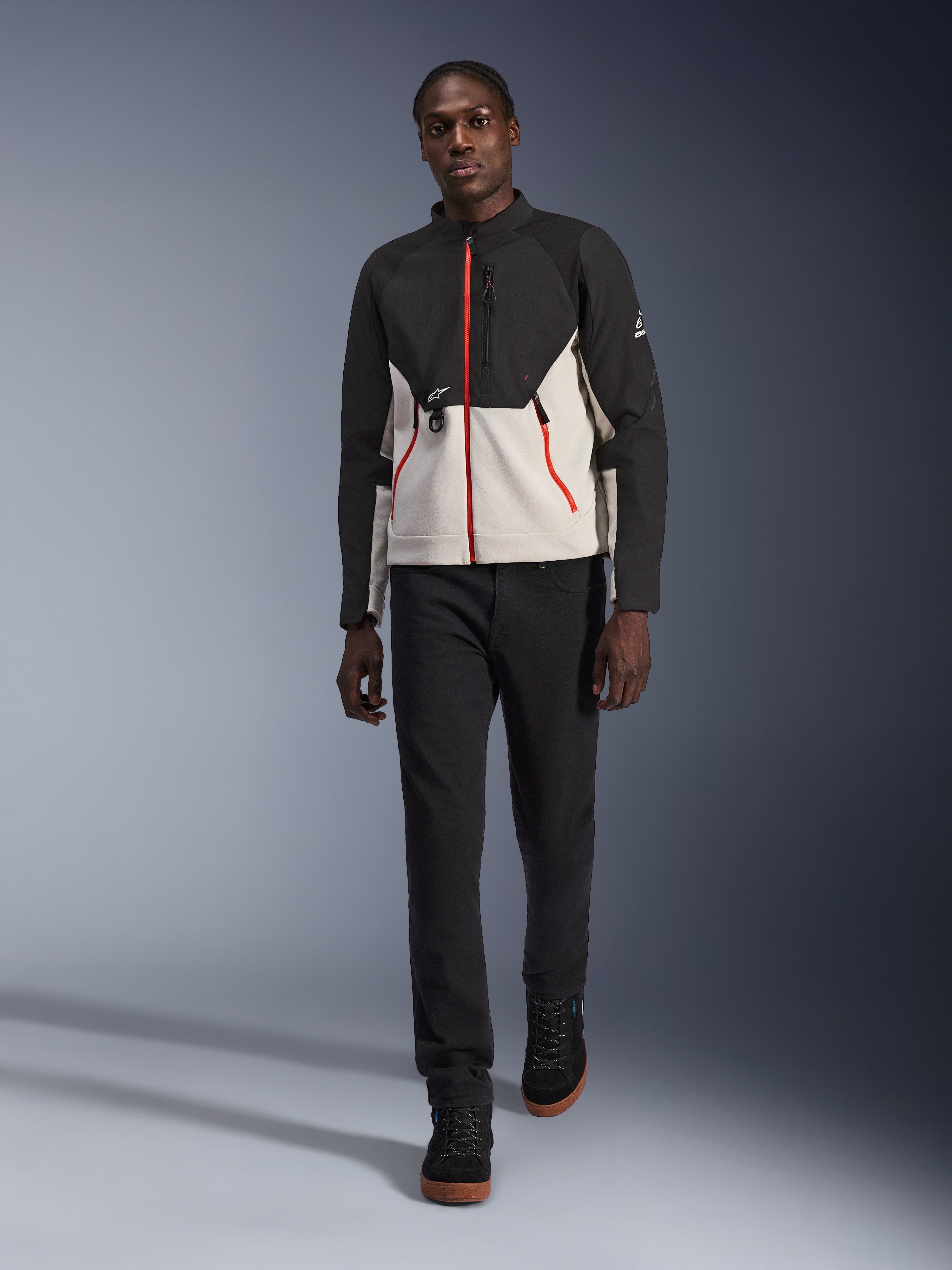 Modello che indossa la giacca Alpinestars Provoke, giacca da moto urbana in nero e grigio metallo con dettagli delle zip rossi, abbinata a pantaloni neri e scarpe alte nere, abbigliamento protettivo moderno per la guida urbana