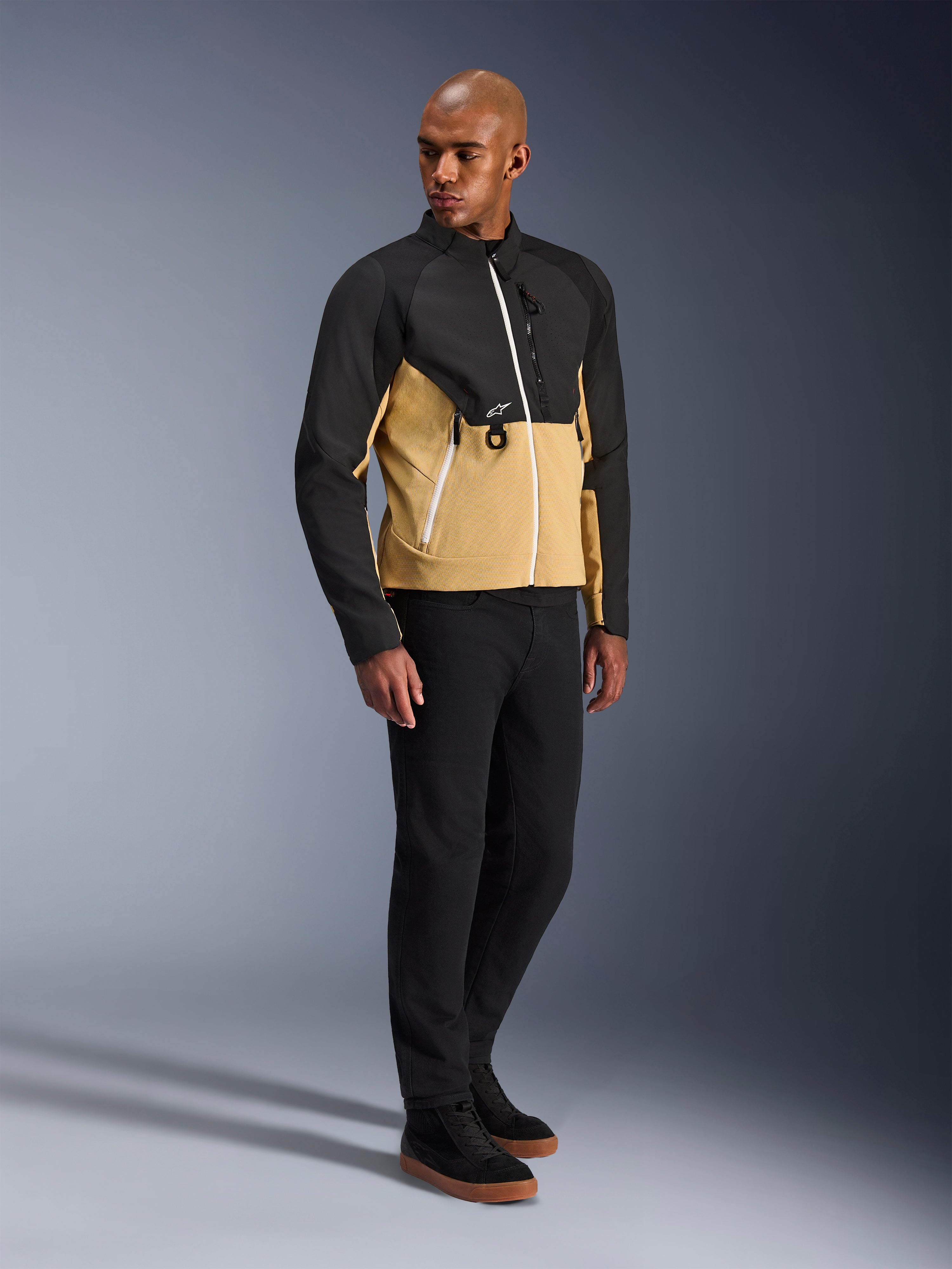 Giacca Alpinestars Provoke, giacca da moto urbana, Black Camel, indossata da un modello con pantaloni neri e sneakers, design bicolore in tessuto con parte superiore nera e parte inferiore color cammello, dettagli zip bianchi, abbigliamento da moto urbano contemporaneo