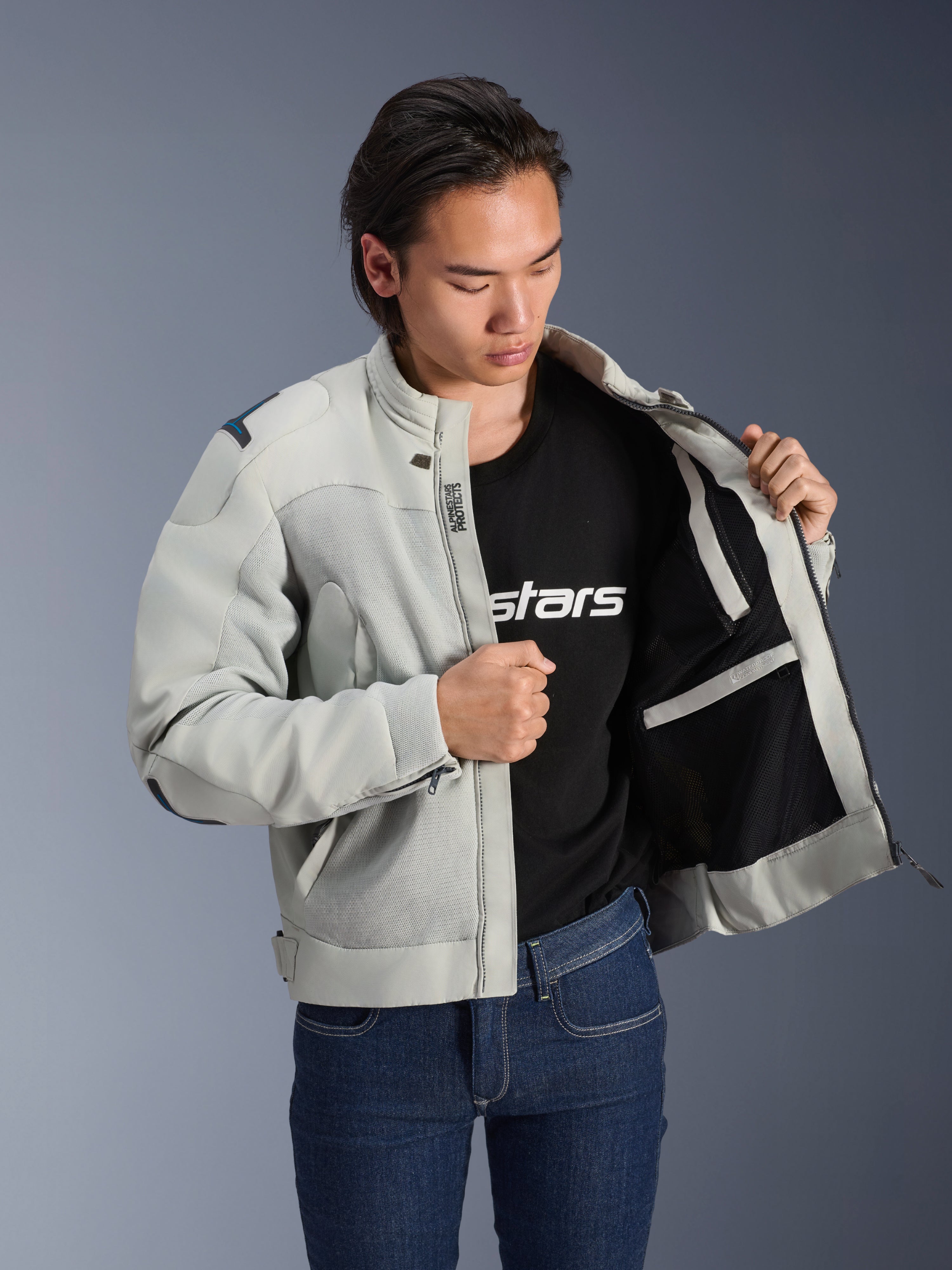 Giacca Alpinestars Circal-1 Air, Metal Gray, mostrata aperta per esporre la fodera interna in mesh e i dettagli delle tasche, indossata da un modello con t-shirt nera con logo e jeans blu, stile urban motorcycle