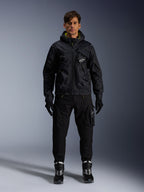 Modello che indossa la Giacca Alpinestars Mogress Air, giacca in tessuto nero con cappuccio e dettagli lime punch, abbinata a pantaloni utility neri, guanti neri e stivali da moto neri e bianchi, design streetwear ispirato al motorsport urbano