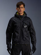 Alpinestars Mogress Air Jacket, giacca da moto urbana, nero con accenti Lime Punch, indossata da un modello con pantaloni da guida e guanti neri, design d'ispirazione utility con cappuccio e logo a stella bianco sul petto, abbigliamento tecnico leggero per la guida su strada