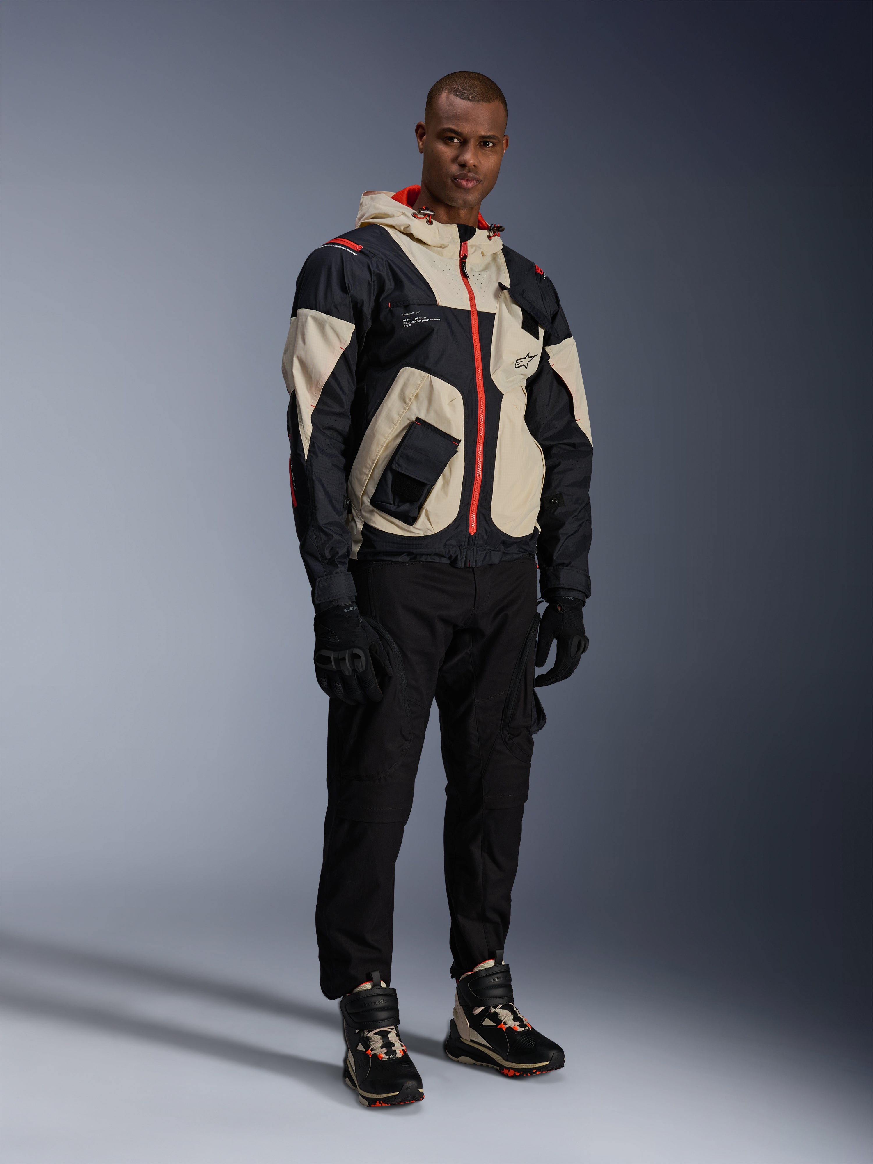 Uomo in abbigliamento completo da moto urban, con scarpe Alpinestars Speedstreet in Black Almond Hot Orange e giacca Mogress Air in nero e crema, pantaloni e guanti neri coordinati, outfit protettivo di ispirazione streetwear per la guida su strada