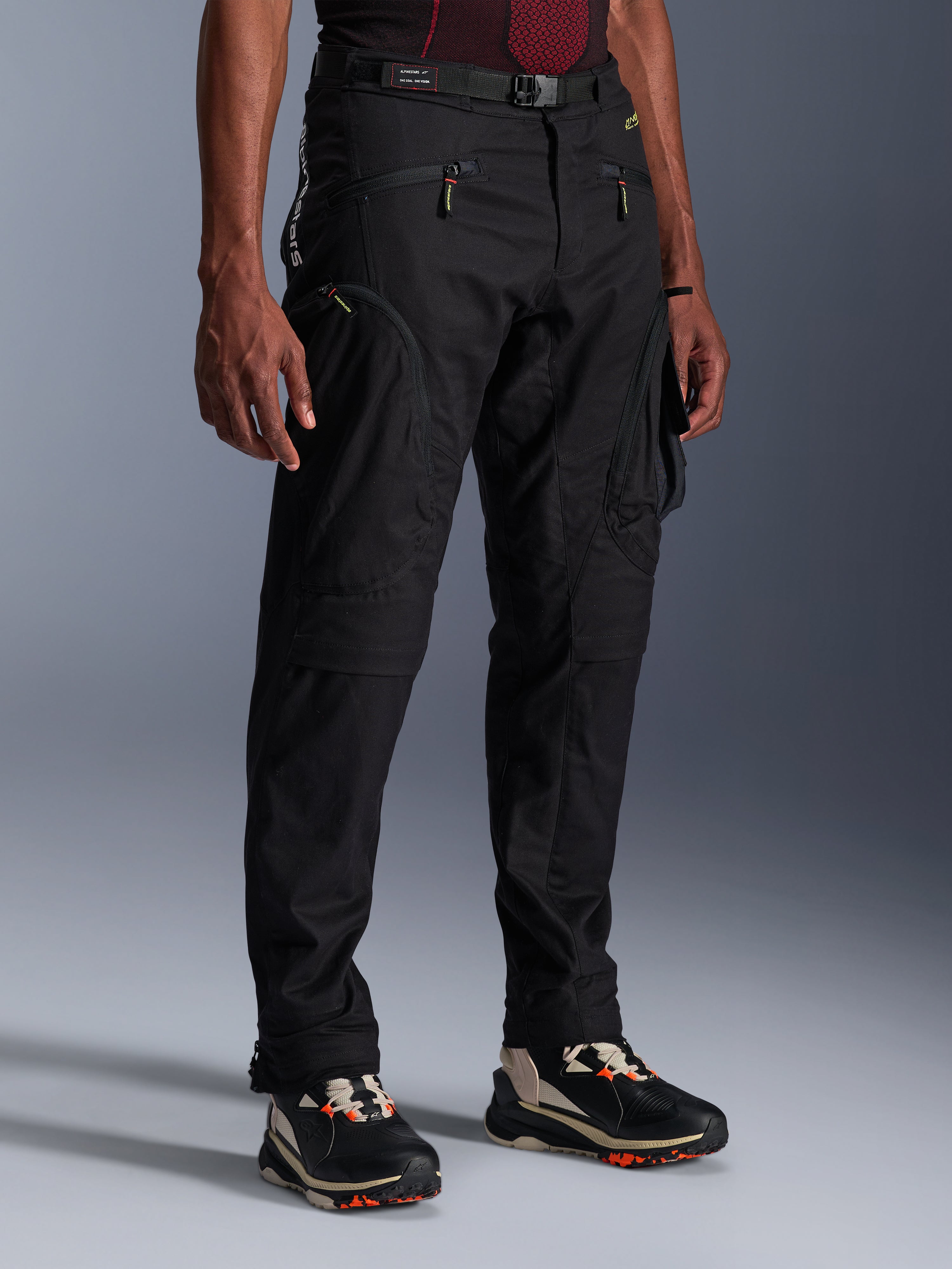Pantaloni Alpinestars Acteon, pantaloni da moto neri, indossati da un modello, con silhouette moderna affusolata, tasche cargo con zip, cintura regolabile in vita e sneakers tecniche, abbigliamento da moto urbano