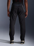 Pantaloni Alpinestars Acteon, pantaloni moto urban, nero, vista posteriore con vestibilità affusolata, branding bianco sulla parte superiore delle gambe e logo giallo sulla parte inferiore del polpaccio, fondo gamba regolabile con zip, indossati con sneaker color crema