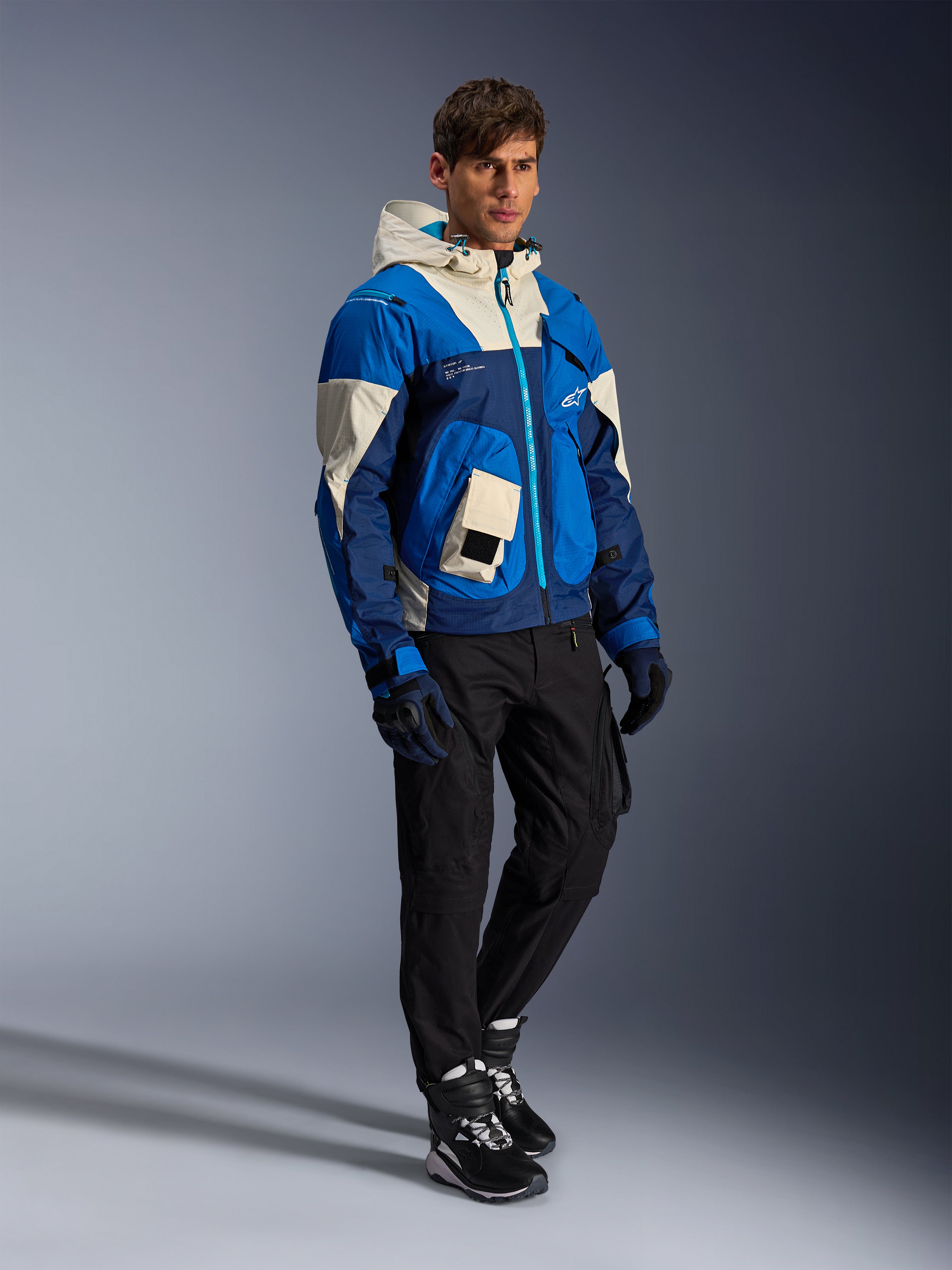 Giacca Alpinestars Mogress Air, giacca da moto urbana, Blue Almond con pannelli crema e blu navy, dotata di cappuccio e tasche utility, indossata con pantaloni da moto neri, guanti e stivali, abbigliamento protettivo contemporaneo ispirato allo streetwear.