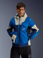 Modello che indossa la giacca Alpinestars Mogress Air in Blue Almond, giacca da moto urbana con blocchi di colore blu acceso e blu navy, accenti crema sul cappuccio e sulle tasche, tessuto tecnico ripstop con tasche utility, streetwear moderno ispirato al motorsport