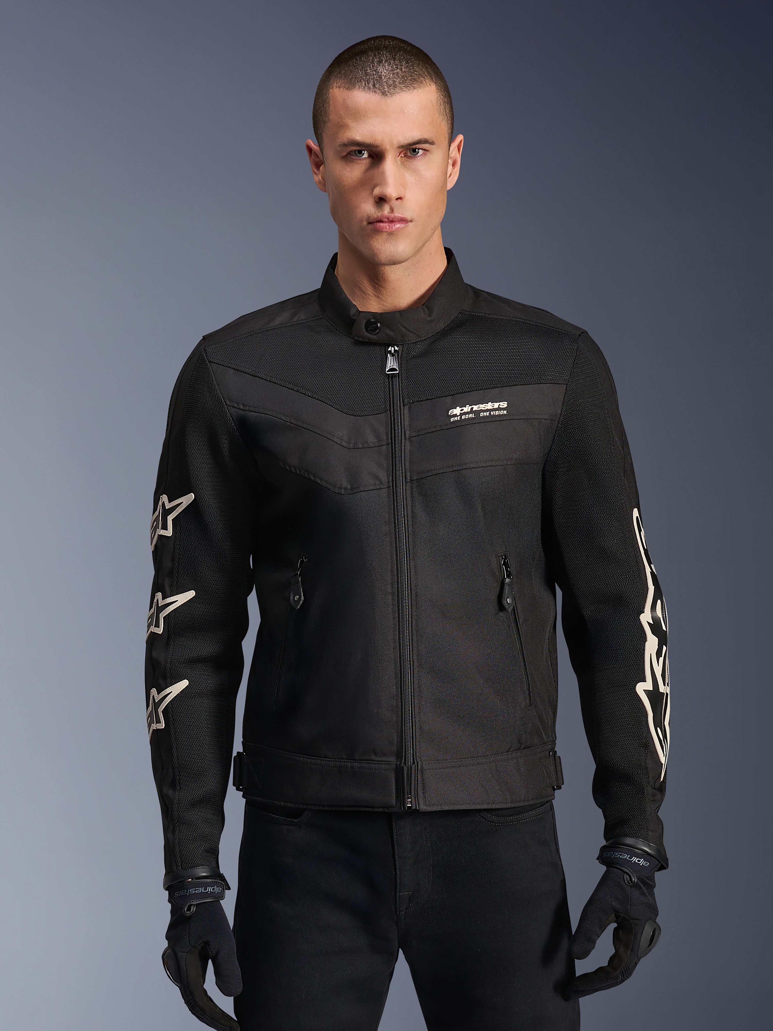 Alpinestars T-Dyno Air Jacket, giacca da moto in tessuto nera, con grafiche a stella bianche sulle maniche e logo sul petto, pannelli in mesh per la ventilazione, vestibilità biker d'ispirazione vintage, indossata con guanti e pantaloni neri