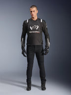 Giacca Alpinestars T-Stunt Air, giacca da moto nera e bianca, indossata con pantaloni da moto neri, guanti e stivali, caratterizzata da logo Alpinestars bianco sul petto e sulle maniche, design in tessuto a taglio sportivo con pannelli in mesh per la ventilazione