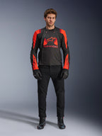 Giacca Alpinestars T-Stunt Air, Nero Rosso Fluo e Rosso Scuro, indossata da un modello con jeans da moto neri e guanti, caratterizzata da un design modulare 2-in-1 con ampi pannelli in mesh per il flusso d'aria, abbigliamento da moto dal taglio sportivo per la guida su strada