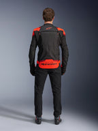 Giacca Alpinestars T-Stunt Air, nero con accenti rosso fluo e rosso scuro, vista posteriore su modello, abbinata a pantaloni da moto e stivali neri, con marchio Alpinestars sul pannello posteriore inferiore, design modulare con costruzione in mesh per la ventilazione.