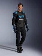 Modello che indossa la giacca Alpinestars T-Stunt Air, nero, blu scuro e azzurro, con evidenti pannelli in mesh per il flusso d'aria, abbinata a pantaloni neri e guanti da moto, giacca da moto dal taglio sportivo per la guida su strada estiva.