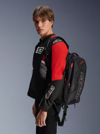 Zaino Alpinestars MM93 City Hunter V2, nero con accenti rossi, indossato da un modello con una giacca da moto MM93 coordinata nera e rossa, con marchio e loghi Marc Márquez, abbigliamento per guida urbana