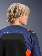 Giacca Alpinestars MM93 T-SPS Air V2, blu navy e nero con accenti rosso fluo, primo piano della parte superiore della schiena con marchio 'MARC MARQUEZ', pannelli in rete traspirante e costruzione in tessuto traforato, indossata da un modello biondo.