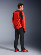 Giacca Alpinestars MM93 T-SPS Air V2 in Rosso Fluo e Nero, vista posteriore di tre quarti su un modello, con marchio Marc Marquez 93 sul colletto e sulla parte inferiore della schiena, abbinata a pantaloni neri e scarpe da moto rosse.