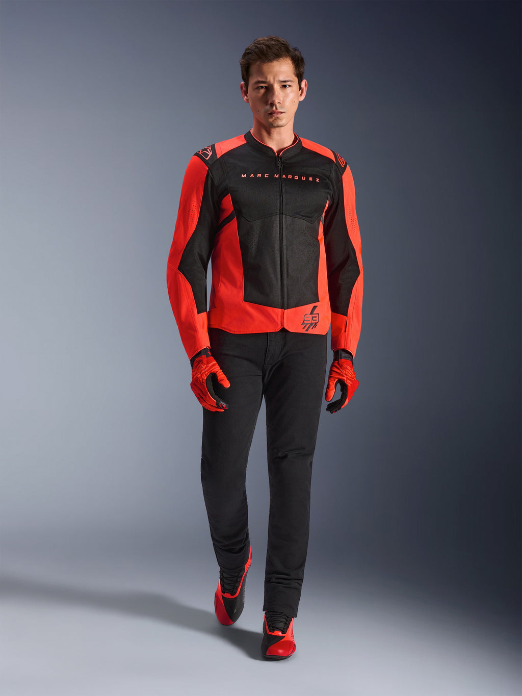 Giacca Alpinestars MM93 T-SPS Air V2, rosso fluo e nero, indossata da un modello con guanti rossi coordinati e pantaloni neri, con marchio Marc Marquez e logo 93, giacca da moto sportiva ventilata per la guida urbana