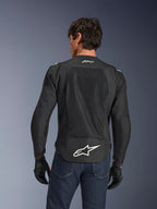 Alpinestars FQ20 T-SPS Air V2 Monster Jacket, nero, vista posteriore con ampi pannelli di ventilazione in rete e logo Alpinestars bianco sulla parte inferiore della schiena, indossata con jeans blu e guanti da moto neri, stile urban sport.