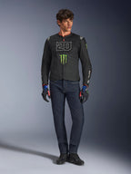 Pilota maschile che indossa la giacca Alpinestars FQ20 T-SPS Air V2 Monster, nera con logo Monster Energy verde e grafica '20' bianca sul petto, abbinata a jeans blu scuro e guanti tecnici da moto, outfit da moto urban sport.