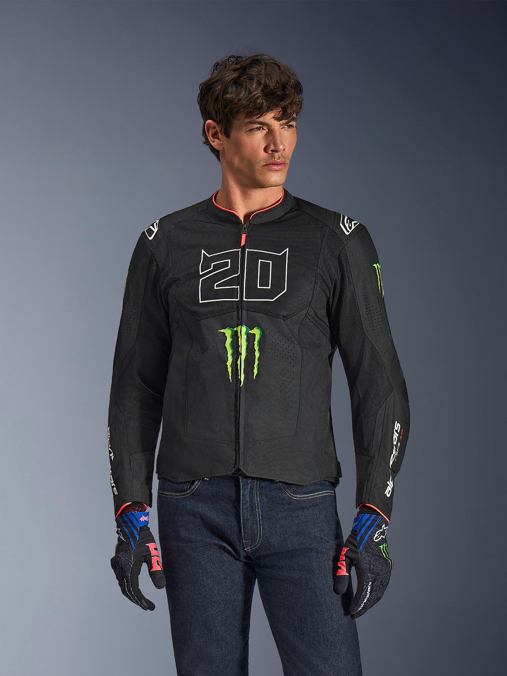 Alpinestars FQ20 T-SPS Air V2 Monster Jacket, giacca da moto nera con grande '20' bianco e logo Monster Energy verde, indossata da un modello maschile con jeans scuri e guanti coordinati, struttura in rete leggera per la guida urbana