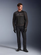 Modello indossa la giacca Alpinestars SMX Air, giacca da moto Black Anthracite con pannelli in rete ventilata e logo grigio sul petto, abbinata a pantaloni neri e guanti protettivi, ambientazione in studio con sfondo sfumato