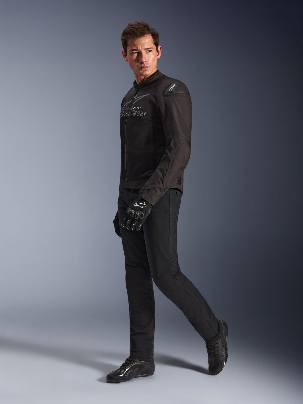 Giacca Alpinestars SMX Air in Black Anthracite, indossata da un modello con pantaloni da moto, guanti e scarpe neri coordinati, inquadratura a figura intera in studio, abbigliamento tecnico sportivo da moto con mesh tecnica e slider sulle spalle