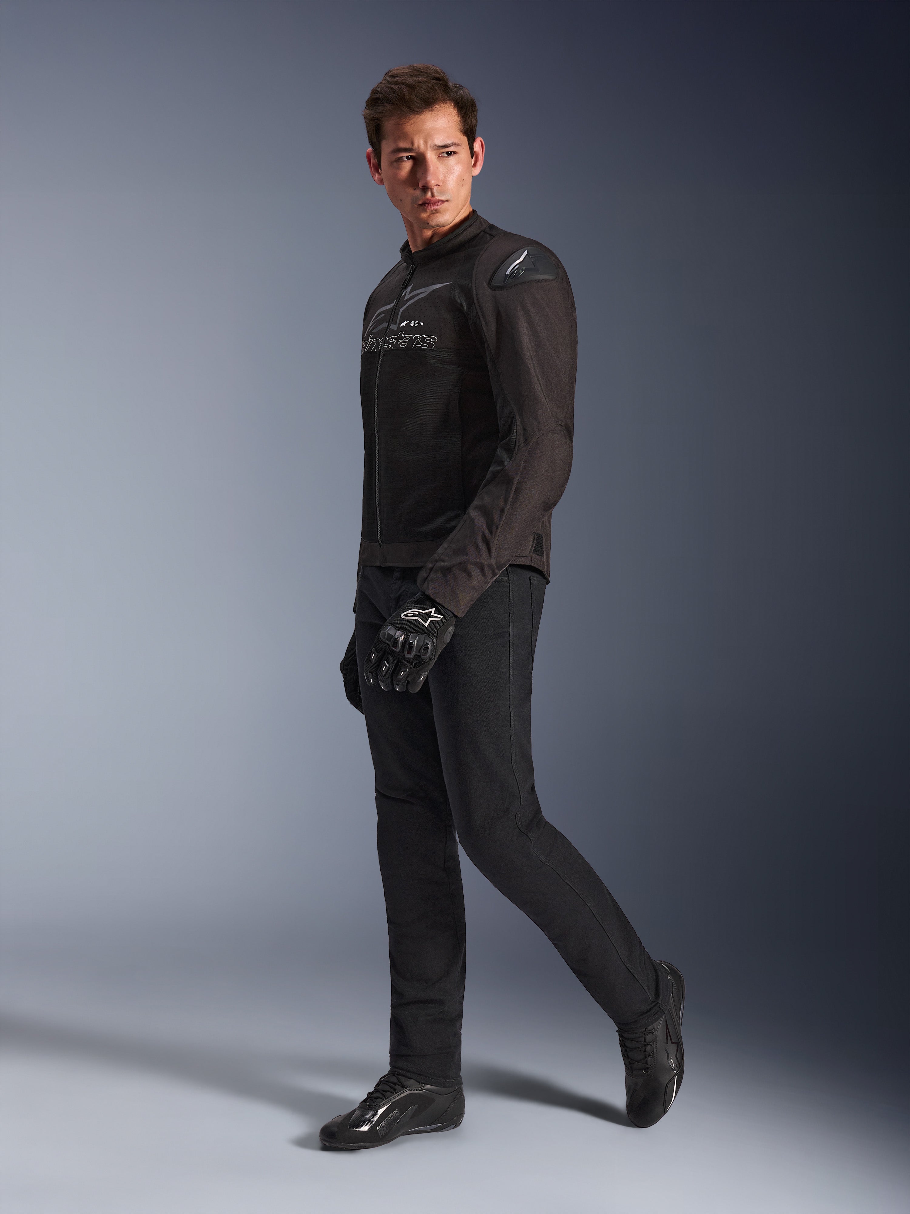Giacca Alpinestars SMX Air in Black Anthracite, indossata da un modello con pantaloni da moto, guanti e scarpe neri coordinati, inquadratura a figura intera in studio, abbigliamento tecnico sportivo da moto con mesh tecnica e slider sulle spalle