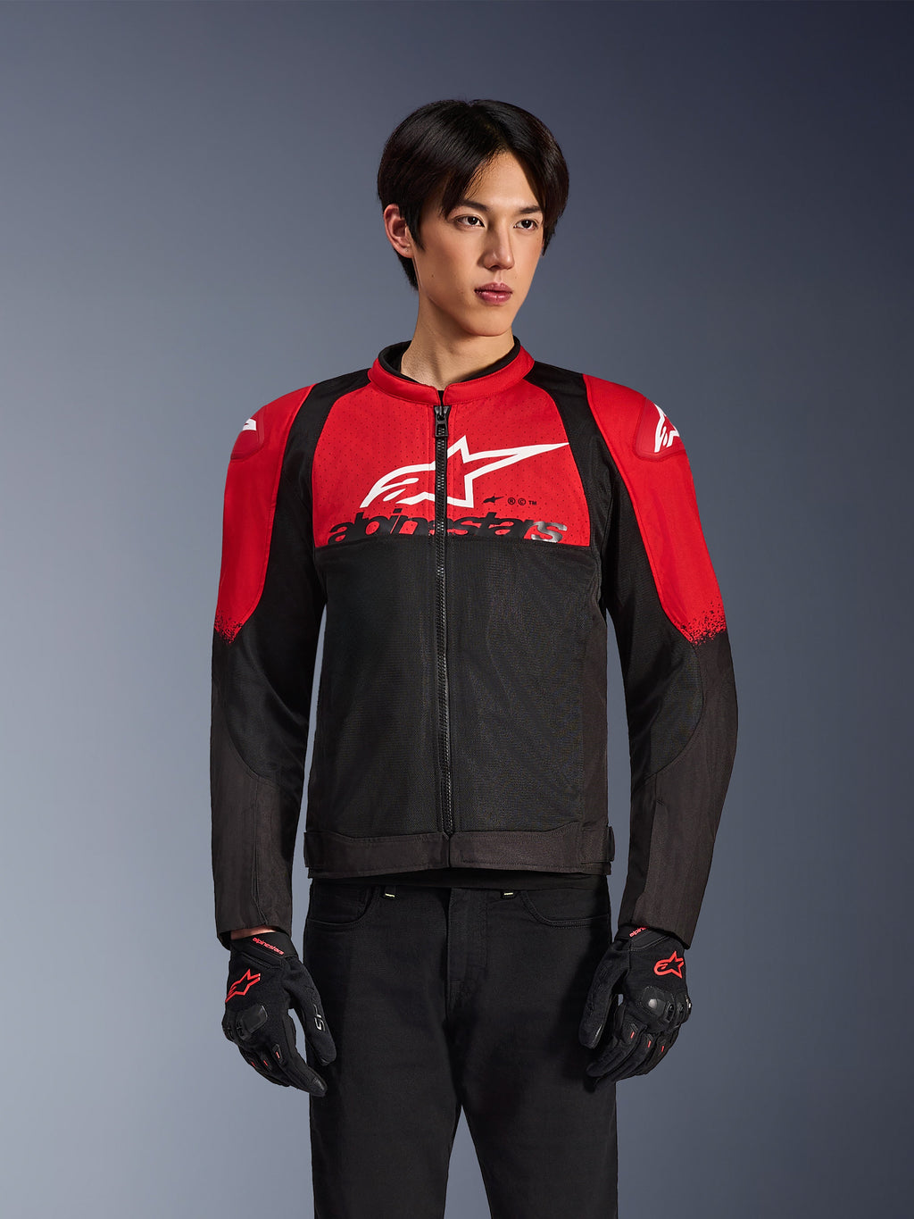 Giacca Alpinestars SMX Air, giacca da moto in rete, rosso acceso e nero, indossata da un modello con guanti da guida neri, con un grande logo bianco sul petto, costruzione in tessuto ventilato con pannelli rossi sulle spalle e maniche nere, abbigliamento sportivo performante per climi caldi